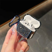 Black glittery airpods case with white earbuds held by a hand