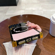 Hand holding a small electronic device with a pink screen on a wooden table.