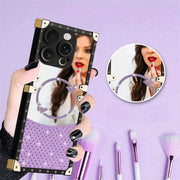 Person holding a phone case with a mirror and decorative elements on a purple background with makeup brushes.