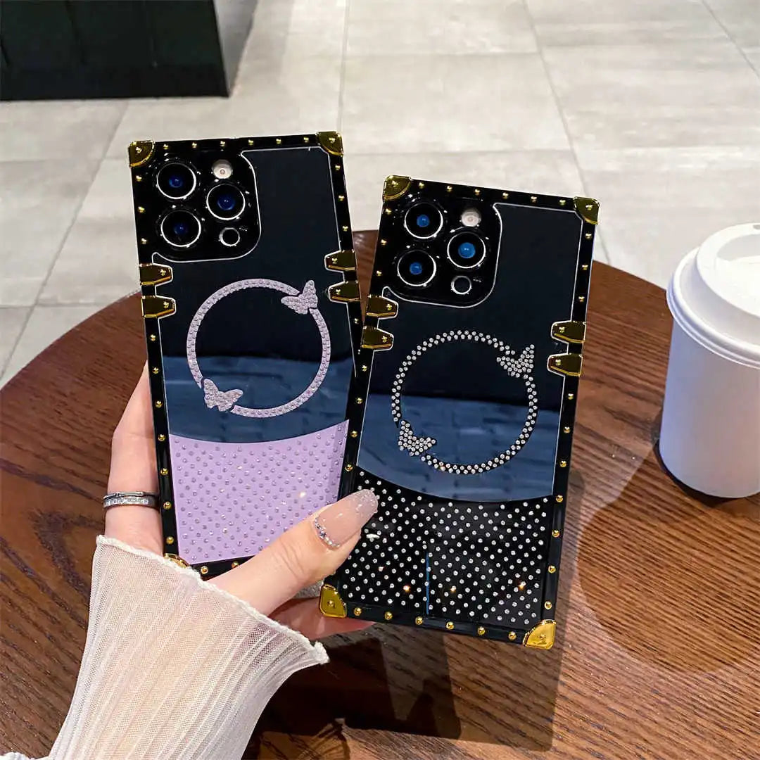 Two black phone cases with decorative patterns held by a hand on a wooden table.