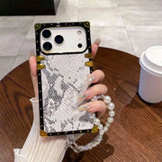 Phone case with snake print and pearl strap held by a hand on a wooden table.