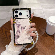 Phone case with snake print and gold accents held by a hand on a wooden table.