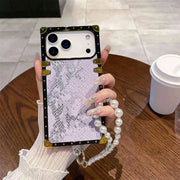 Phone case with lace design and pearl chain held by a hand on a wooden table.