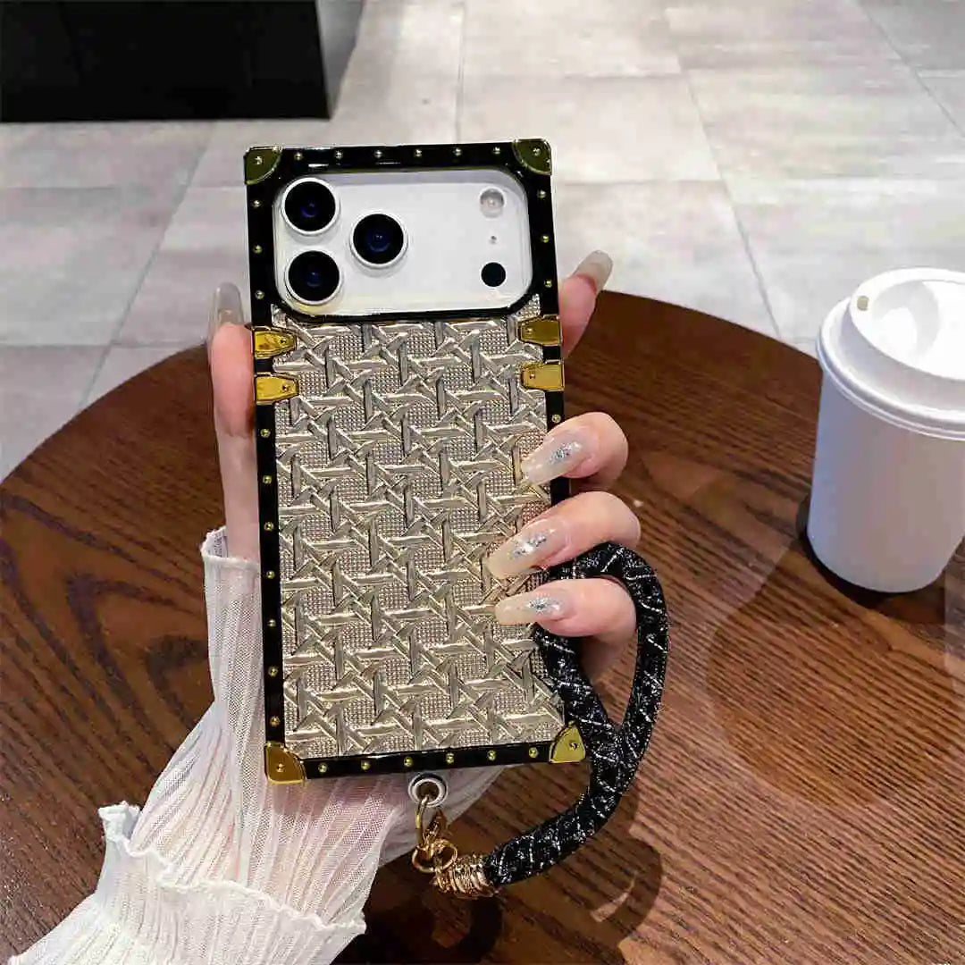 Phone case with decorative pattern and strap held by a hand on a wooden table.
