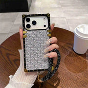Phone case with woven pattern held by a hand on a wooden table.
