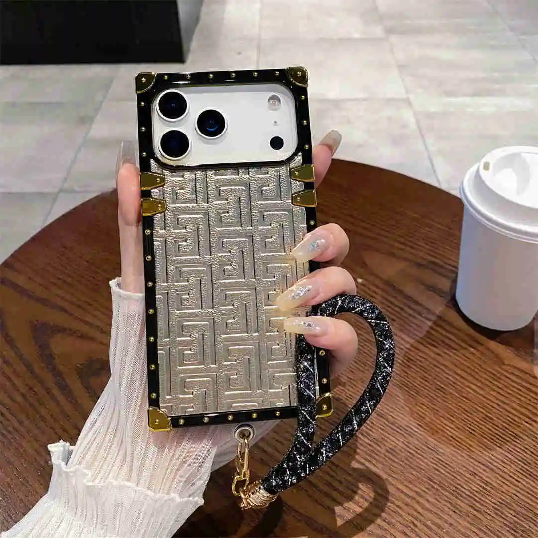 Phone case with geometric pattern and chain strap held by a hand on a wooden table.