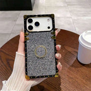 Phone case with decorative ring holder held by a hand on a wooden table.