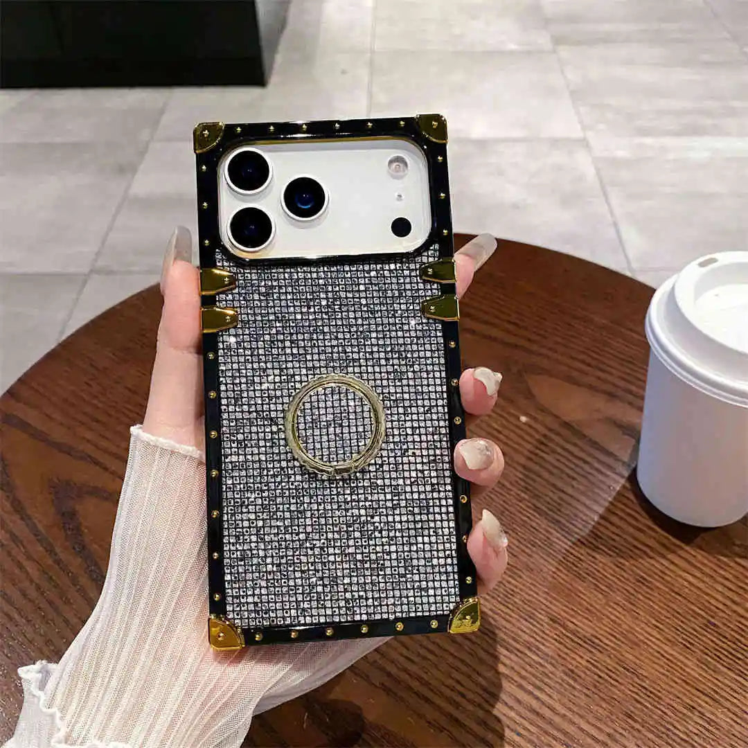 Phone case with decorative ring holder held by a hand on a wooden table.