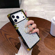 Phone case with rhinestone design held by a hand on a wooden table.