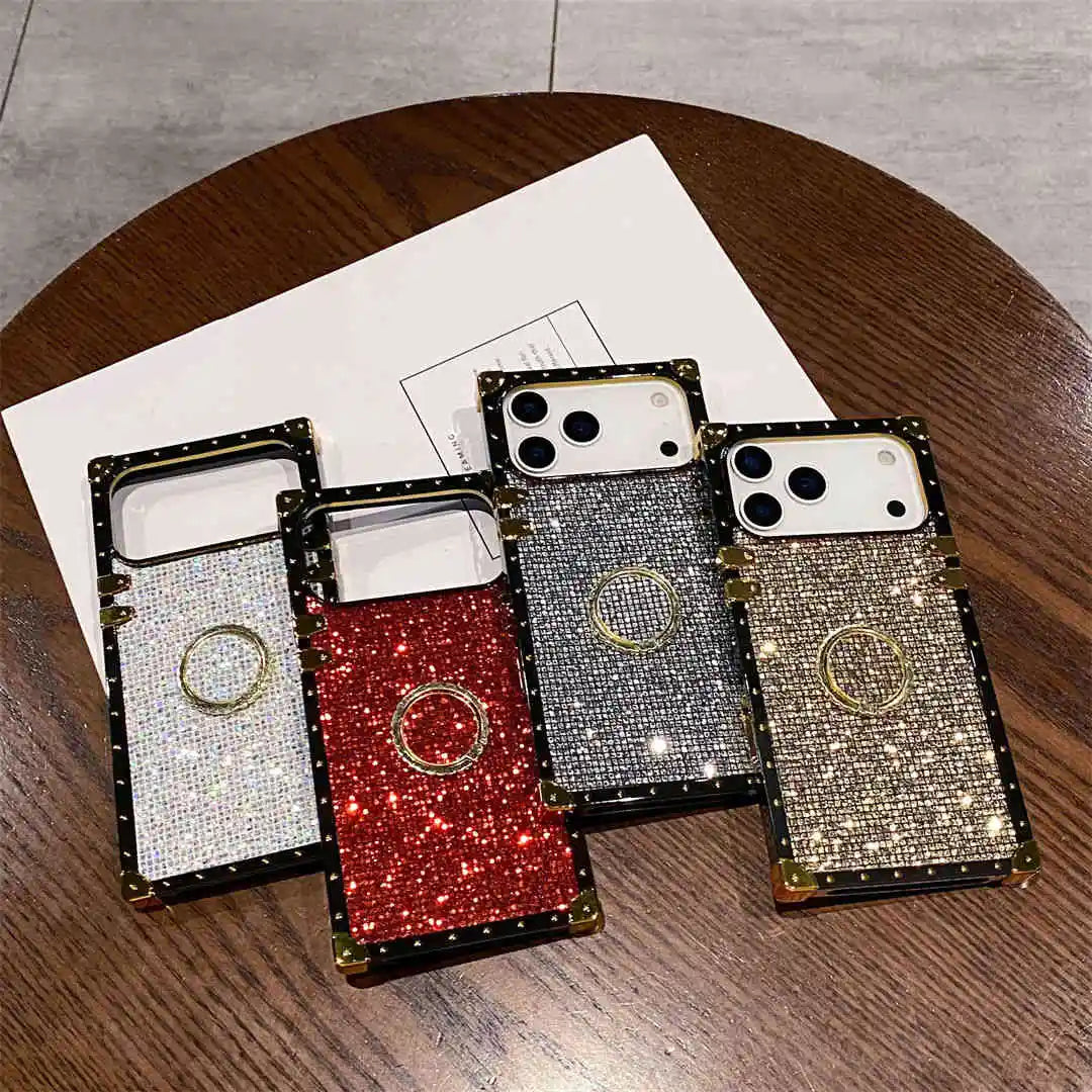Four glittery phone cases on a wooden surface with a paper underneath.