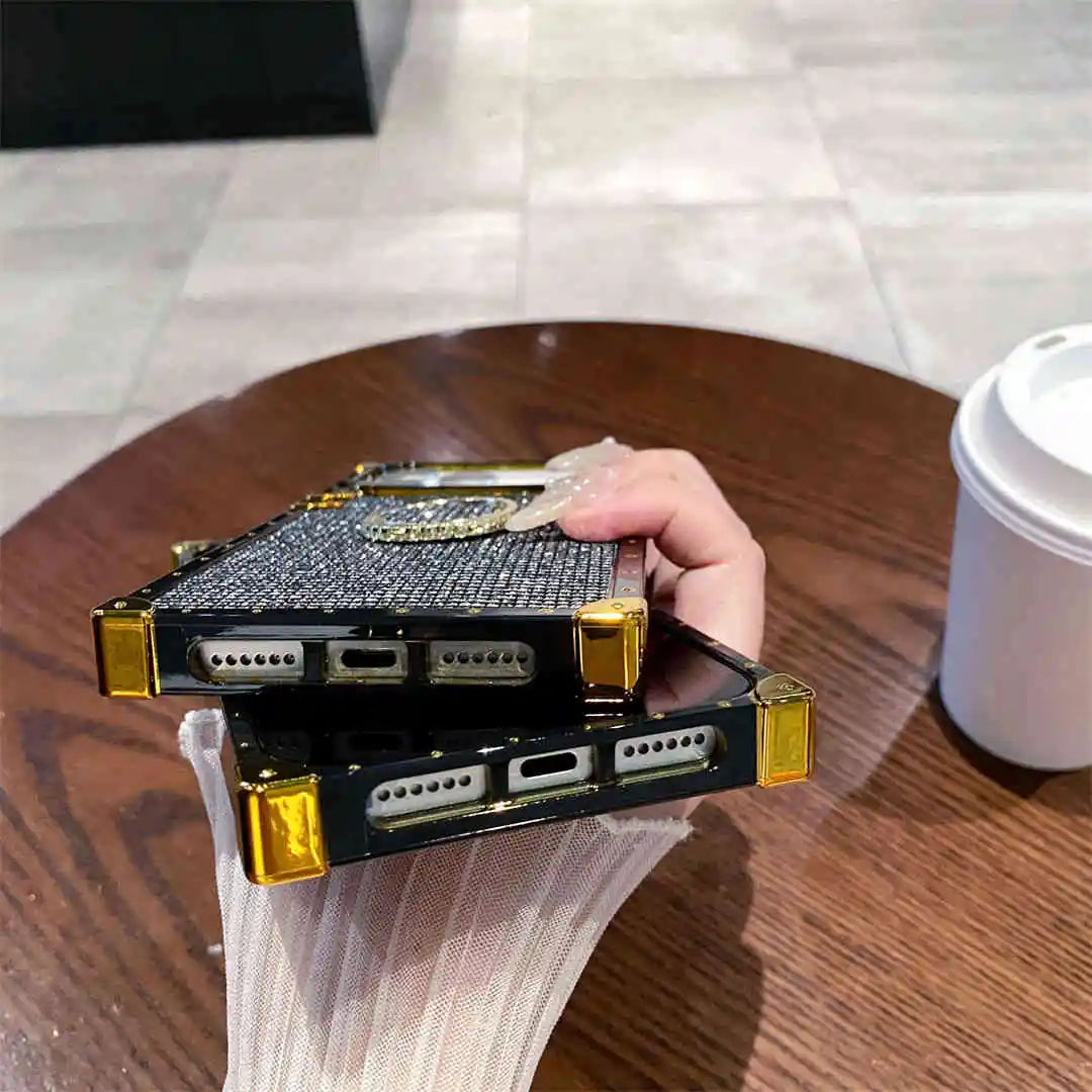Hand holding a small electronic device with gold accents on a wooden table.