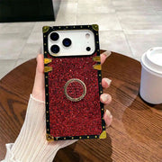 Hand holding a red glitter phone case with gold accents on a wooden table.