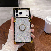 Square phone case with rhinestone design held by a hand on a wooden table.
