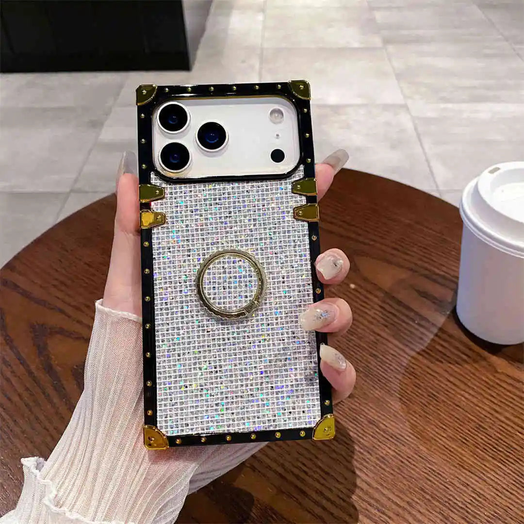 Square phone case with rhinestone design held by a hand on a wooden table.