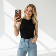 Woman taking a selfie wearing a black top and light blue jeans on a white background