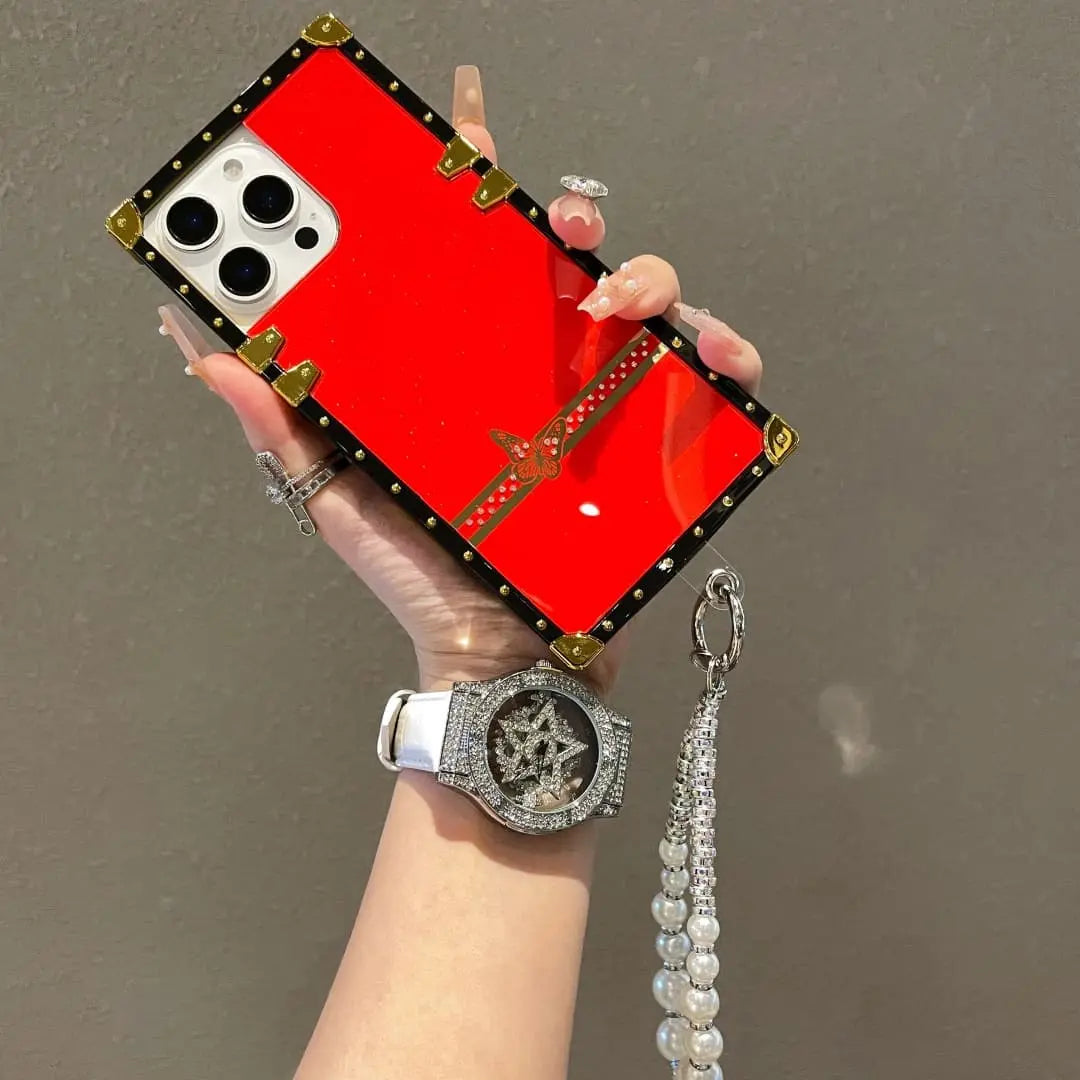 Hand holding a red phone case with decorative elements against a neutral background