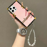 Hand holding a phone with a pink case, wearing a watch and bracelet on a plain background