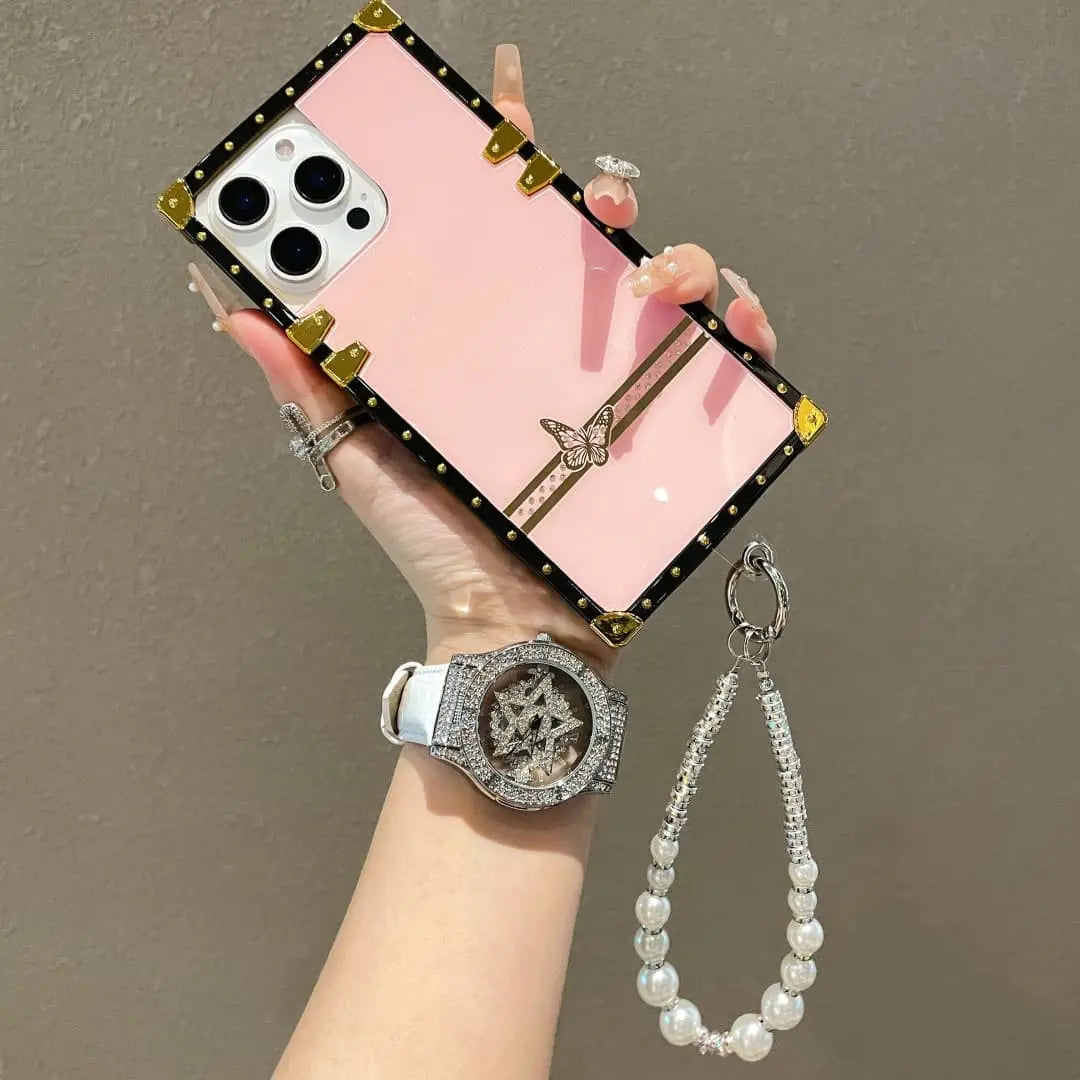 Hand holding a phone with a pink case, wearing a watch and bracelet on a plain background