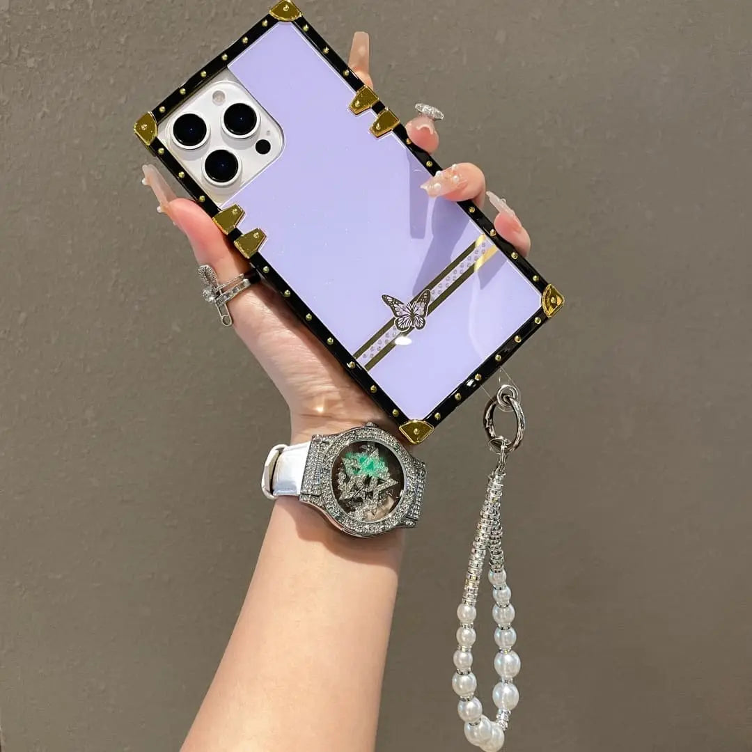 Hand holding a phone with a decorative case and a watch on a plain background