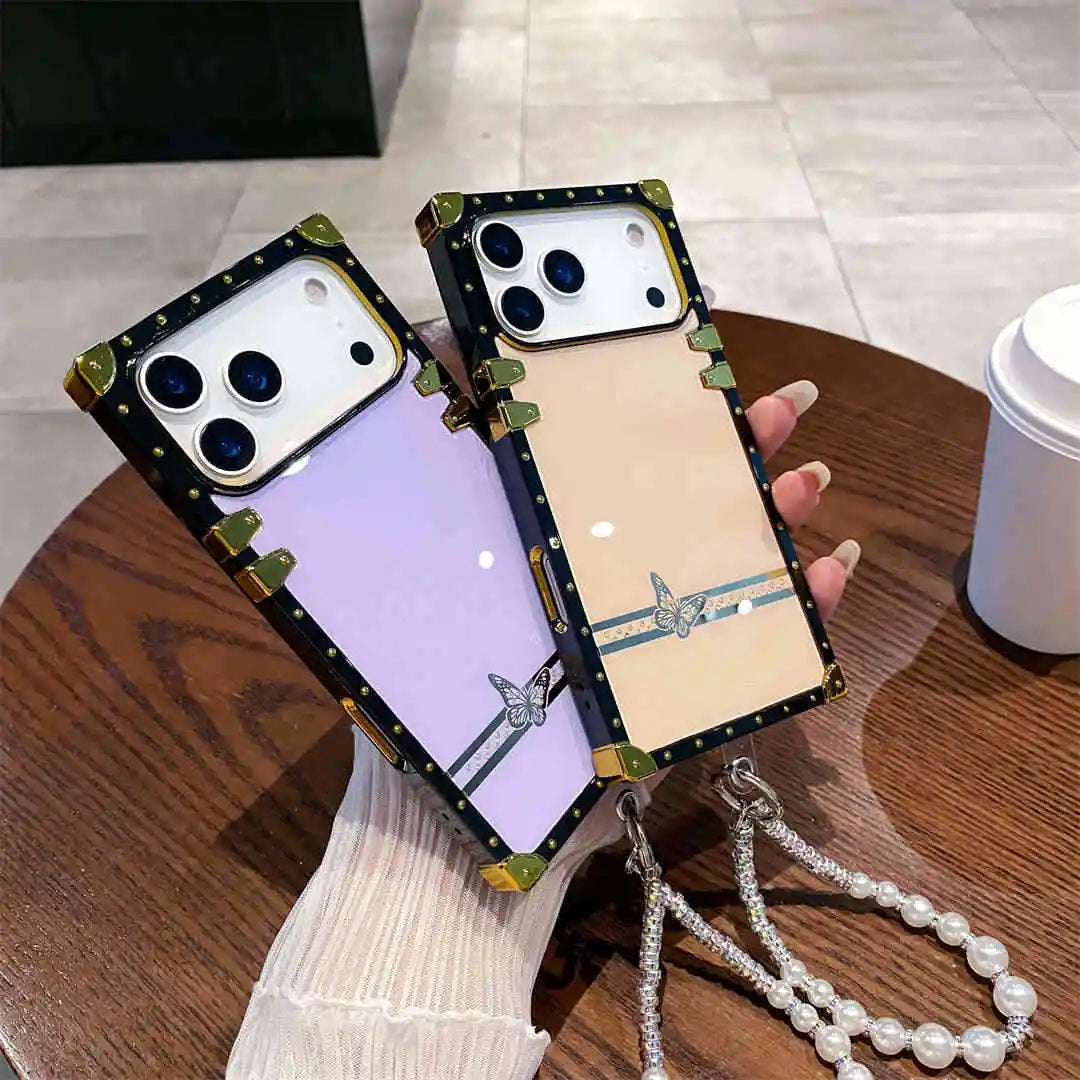 Two phone cases with charms held by a hand on a wooden surface.