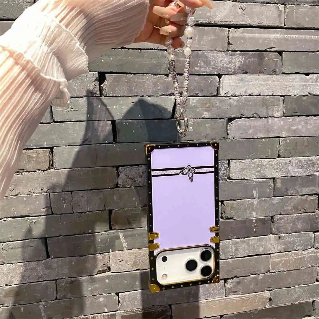 Phone case with a purple back and gold accents held against a stone wall.