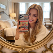 Woman holding a phone with a colorful case in front of a mirror in a bedroom.