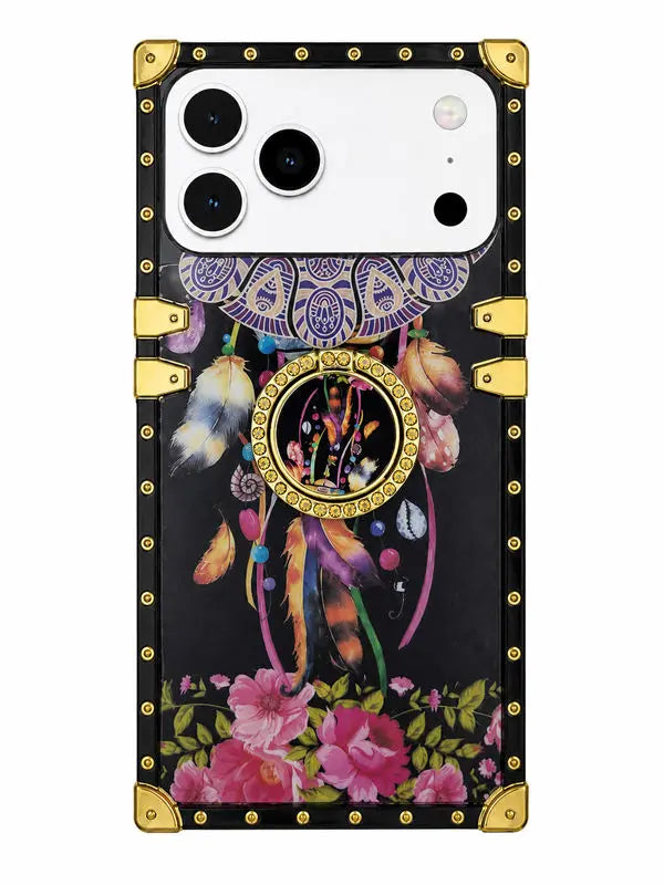 A protective phone case with a black background featuring a dreamcatcher and floral print, finished with gold-tone metal corner protectors and rivets, shown on a white phone.