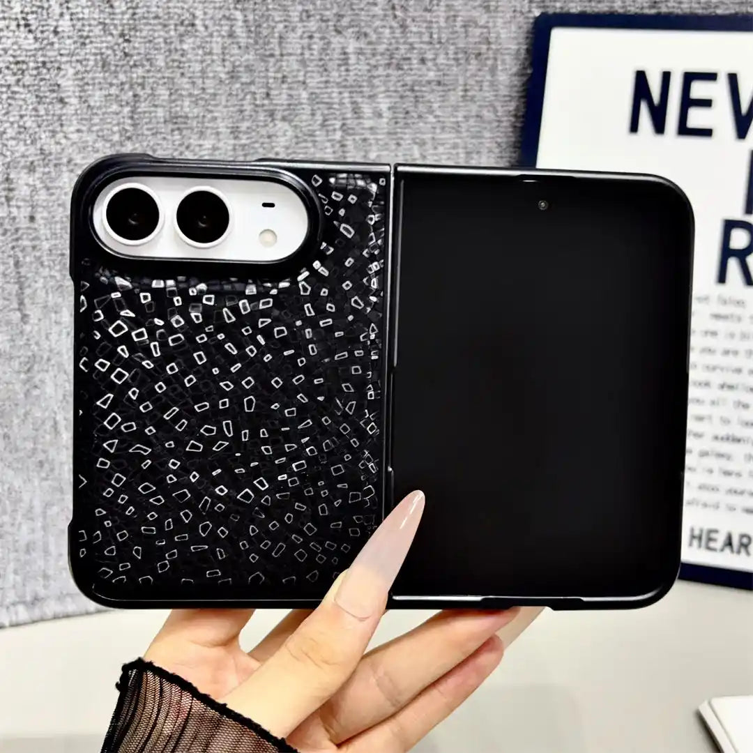 A hand holds a black foldable phone case with a split design: one half has a black background with small white geometric line patterns, and the other half is solid black. The phone inside is turned off.