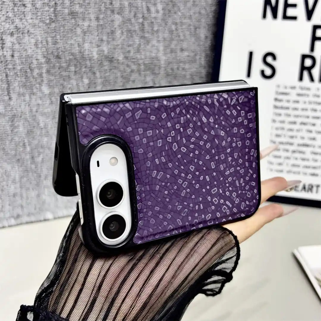 A purple phone case with a small white geometric pattern, shown on a foldable smartphone held in a hand. The case features a black border around the camera cutout.