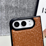 A close-up of a phone case with a textured brown mosaic tile pattern and a black bumper frame, fitted on a smartphone.
