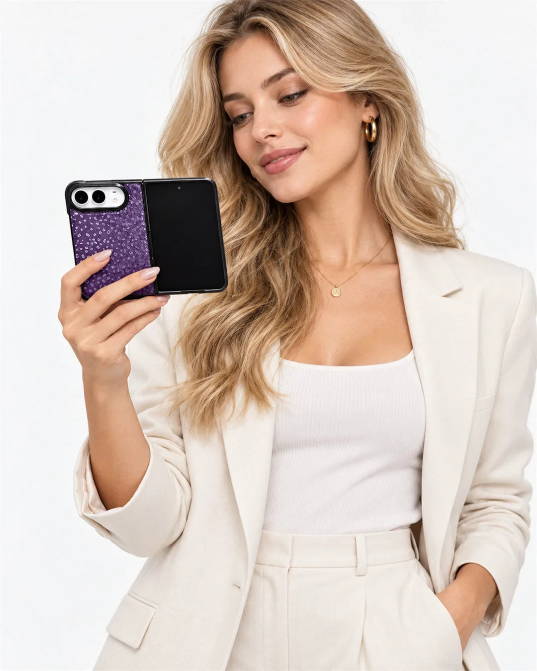 A woman in a cream blazer and white top holds up a iPhone Duo showing a purple glittery case on the back, against a clean white background.