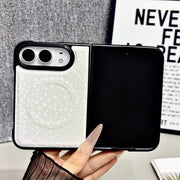 A hand holds a white split-design phone case with a textured circular magnetic ring on the back, shown against a gray textured background with a framed print.