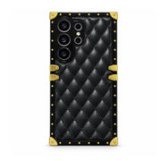 A black quilted leather phone case with gold-tone metal corner protectors and studs, shown on a white background.