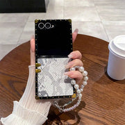 Phone case with decorative chain held by a hand on a wooden table.
