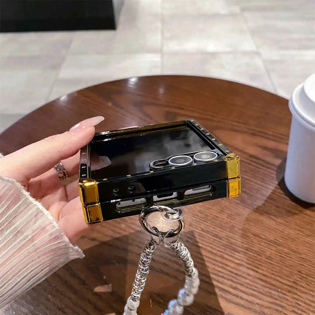Hand holding a black and gold phone case with a camera design on a wooden table.