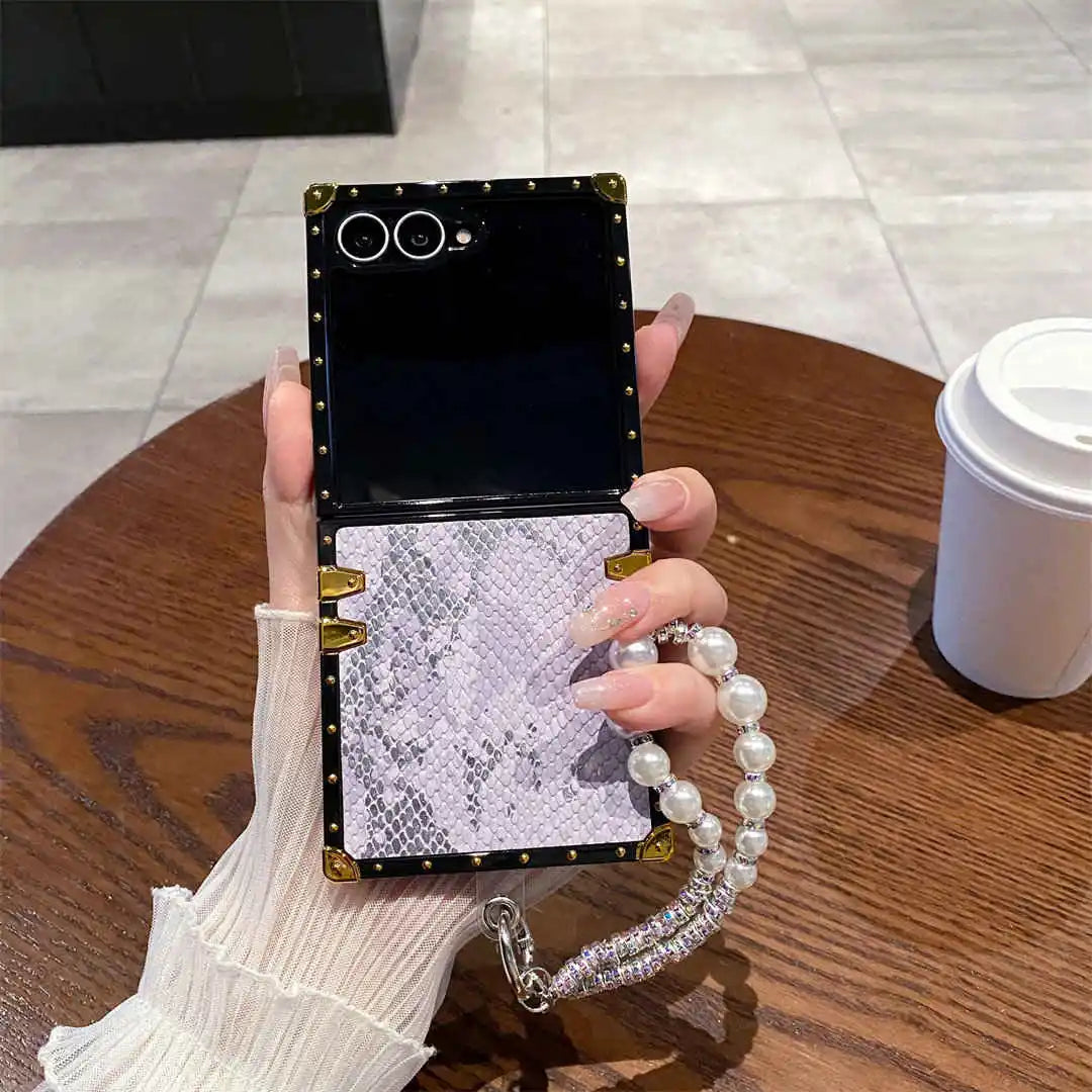 Phone case with decorative chain held by a hand on a wooden table.