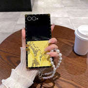 Phone case with yellow snake pattern held by a hand on a wooden table.