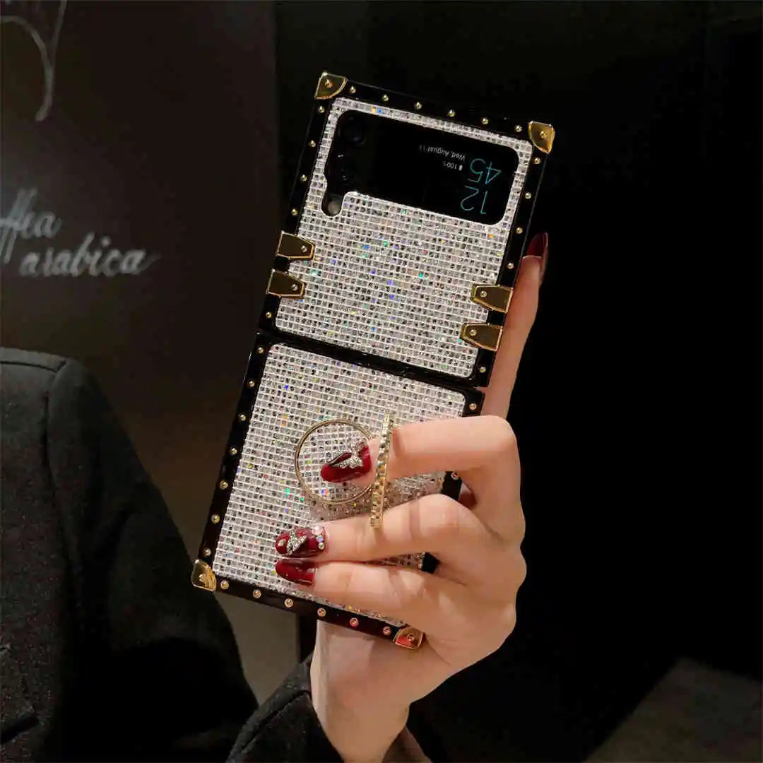 Person holding a phone with a decorative case and ring, against a dark background.