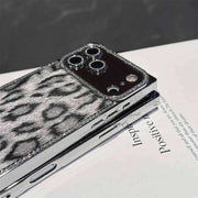 Gray Leopard Chrome Spark iPhone case resting on a book, showing chrome-tone edges and rhinestone trim