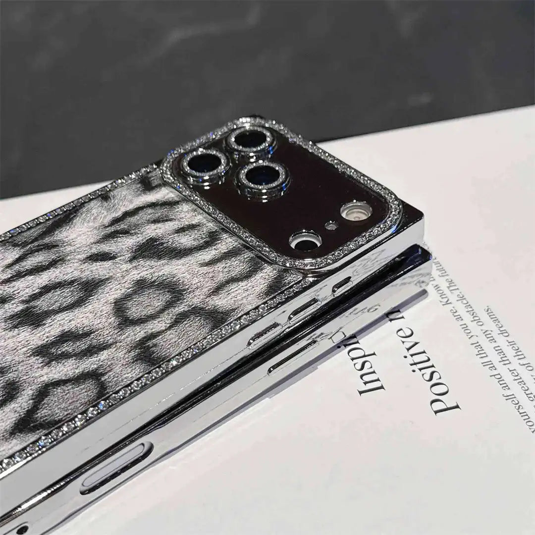 Gray Leopard Chrome Spark iPhone case resting on a book, showing chrome-tone edges and rhinestone trim
