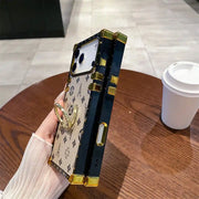 Side view of the beige Paris Monogram Trunk iPhone case showing black frame and gold-tone button cover