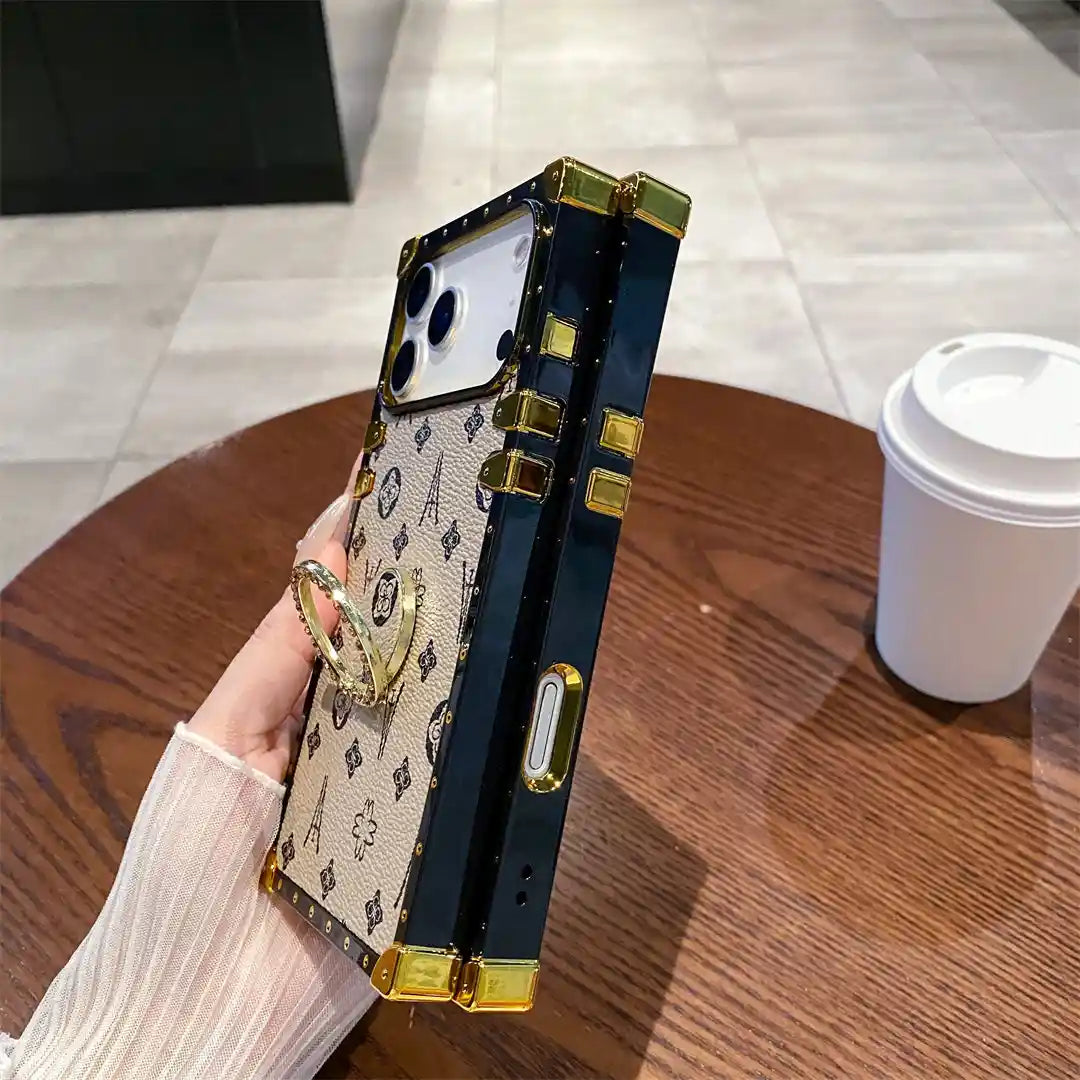 Side view of the beige Paris Monogram Trunk iPhone case showing black frame and gold-tone button cover