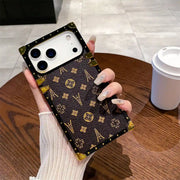 Hand holding the brown Paris Monogram Trunk iPhone case beside a coffee cup