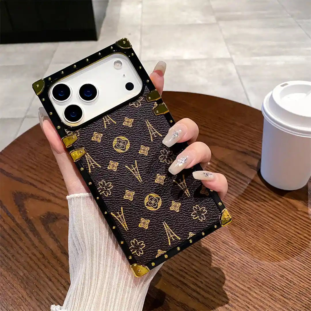 Hand holding the brown Paris Monogram Trunk iPhone case beside a coffee cup