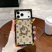 Beige Paris Monogram Trunk iPhone case held upright, showing monogram pattern and ring holder