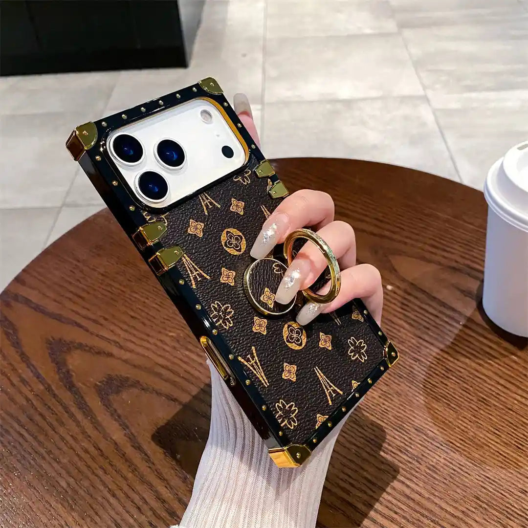 Brown Paris Monogram Trunk iPhone case held using its raised gold-tone finger ring