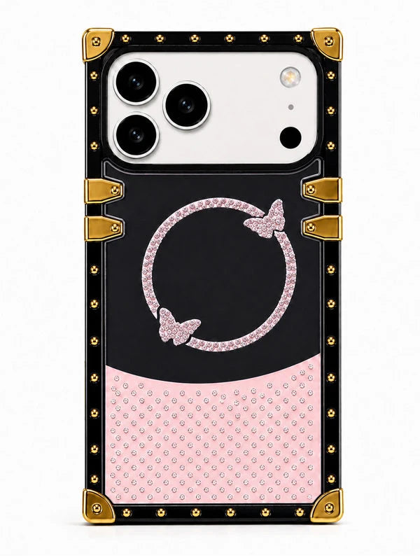 A protective phone case with a black and pink design, featuring a rhinestone-embellished circular motif with butterfly details and gold-tone corner protectors and studs, shown on a white background.