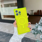 A hand wearing a white sleeve holds a translucent neon yellow-green phone case with a MagSafe ring, photographed outdoors near a window and a small tree.