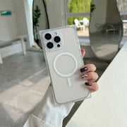 A hand holding a clear MagSafe-compatible phone case with a white magnetic ring, fitted on a light-colored smartphone, set against a bright, modern indoor background.