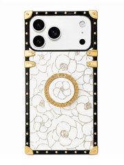 A luxury phone case featuring a white background with an elegant gold floral pattern, framed by a black border adorned with gold studs and corner protectors. A circular gold pop socket is attached to the center back.
